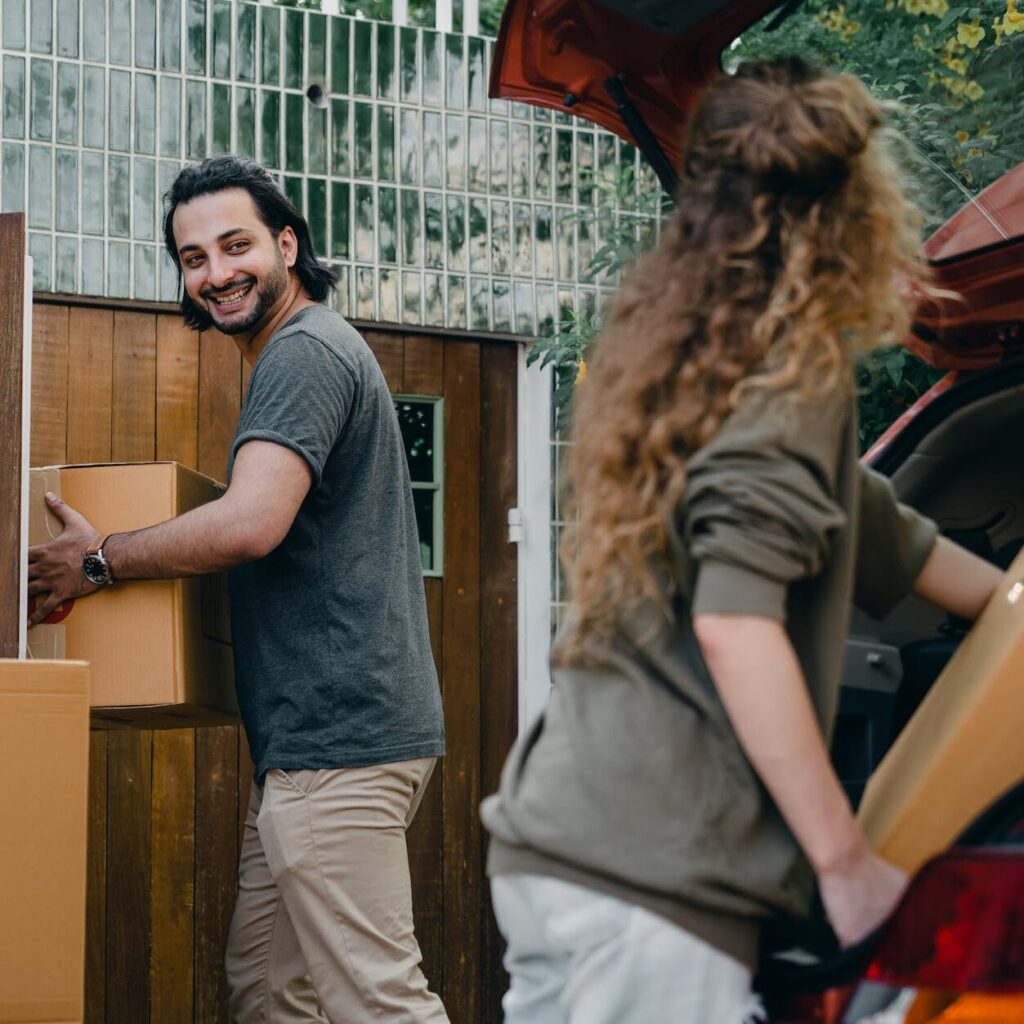 happy couple unloading automobile while moving apartment in summer day