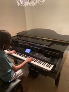 A young man playing an electric piano with focused expression, fingers gliding over the keys in a well-lit room. The piano is sleek and modern, and music sheets are visible on the stand.