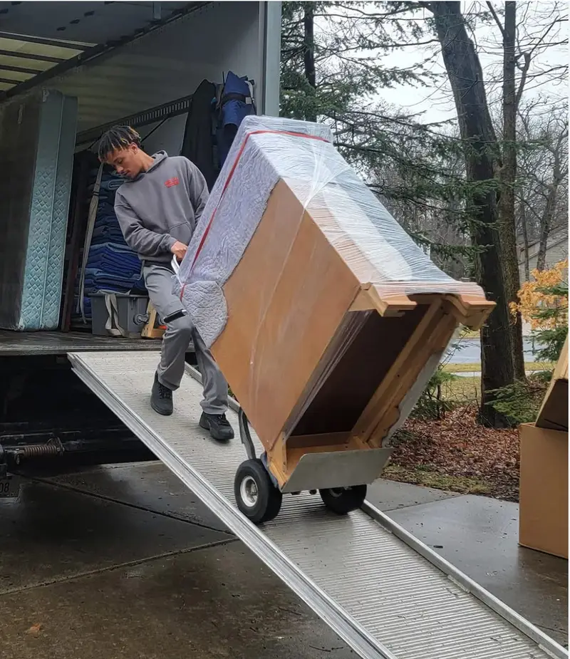 Piano mover guiding a protected upright piano down a truck ramp